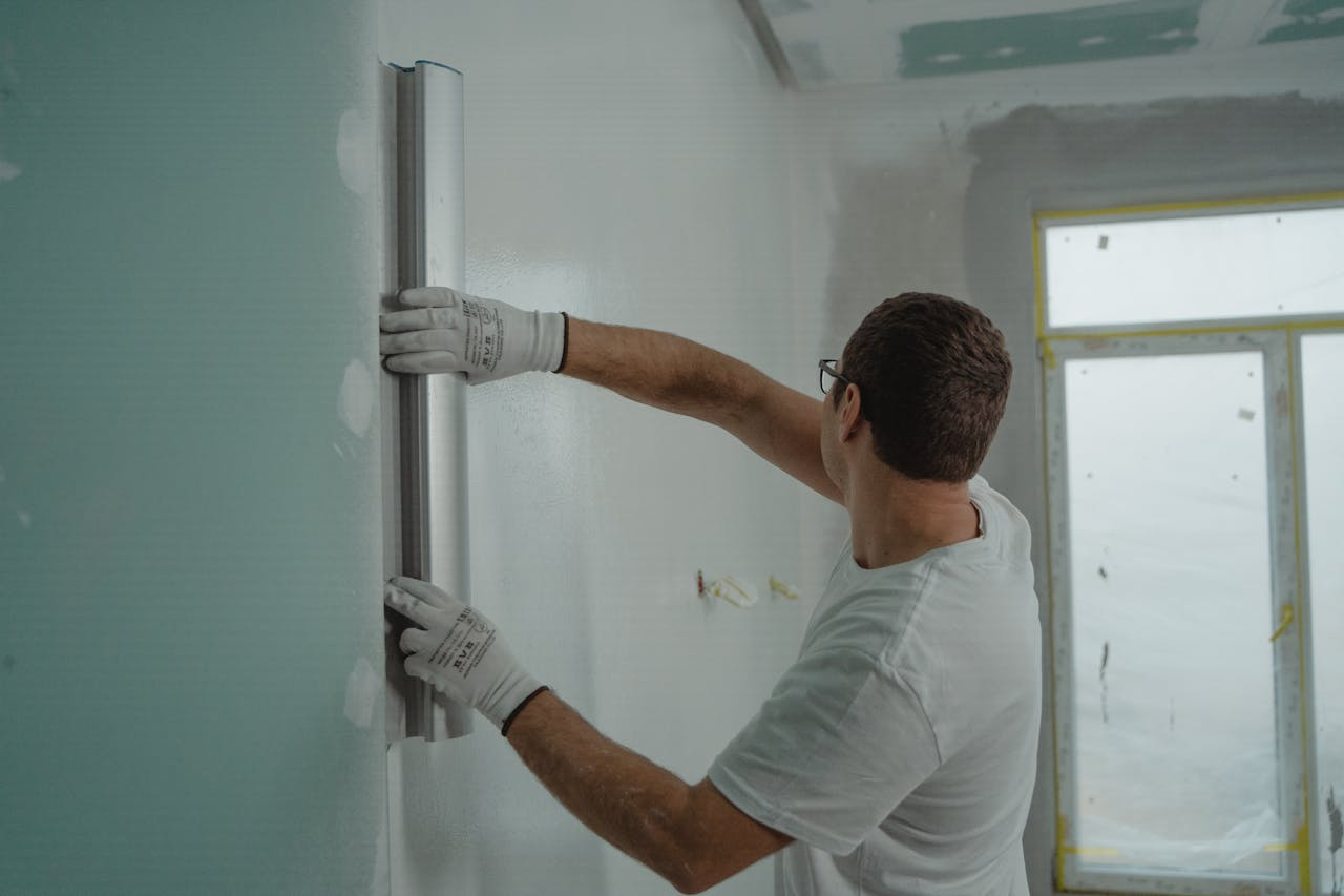 services-04 A man in a white shirt and gloves using a metal ruler for indoor wall renovation work.